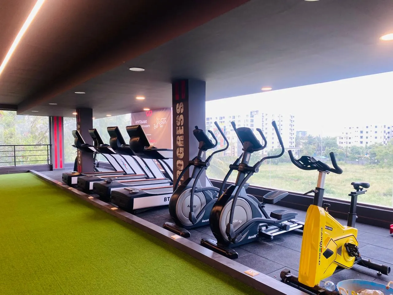 Treadmills, cross trainers and a turf track beside floor to ceiling windows at Swaasthya